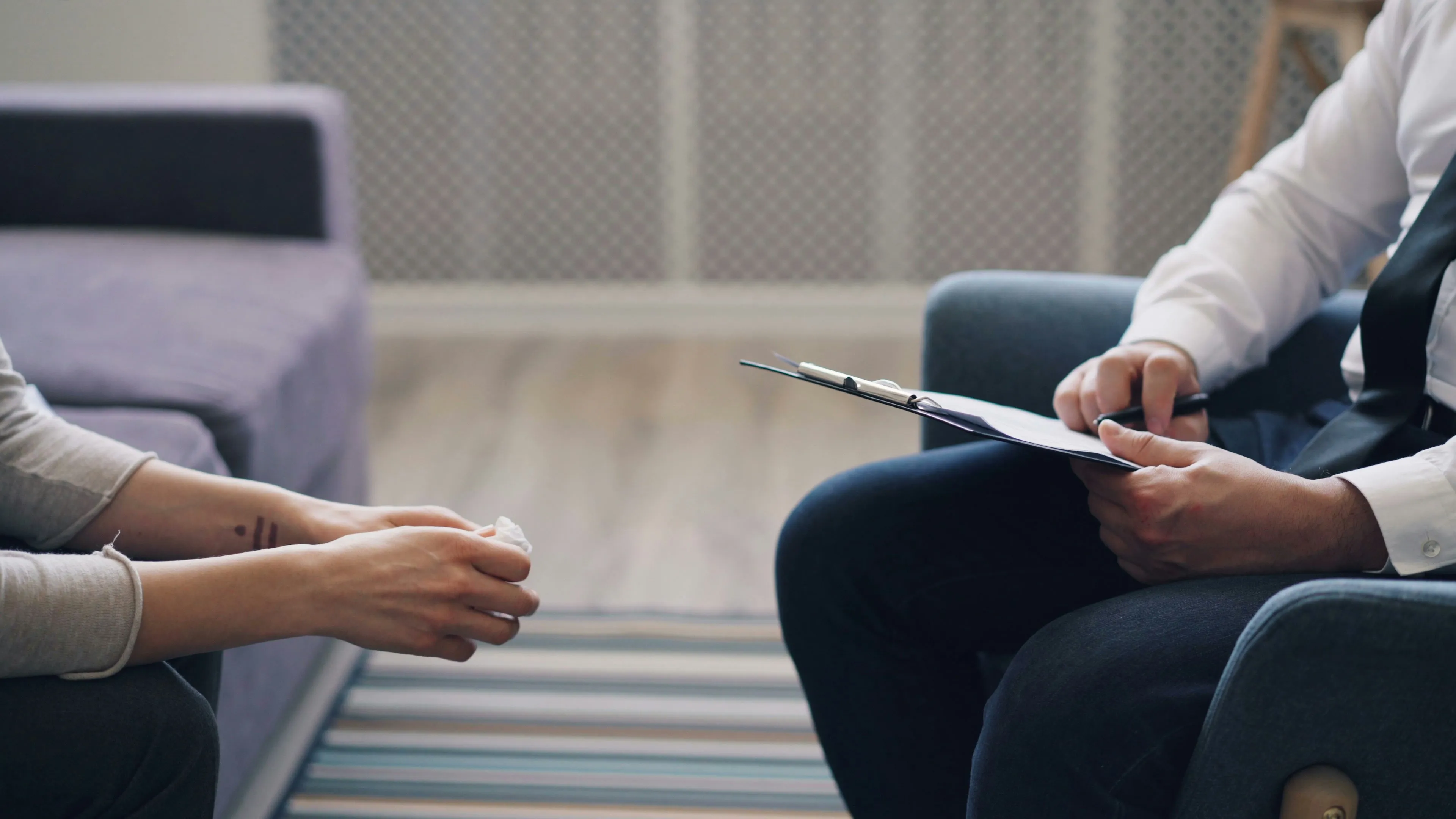 Therapist holding a clipboard across from a patient with a tissue during an ERP therapy consultation. BNBA